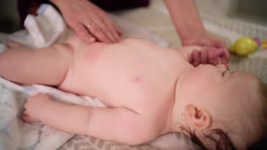 Bebek sırt üstü yatarken bir yetişkin onlara masaj yapıyor ve hareket egzersizleri yapıyor.