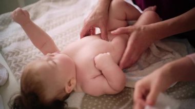 Bebek sırt üstü yatarken bir yetişkin onlara masaj yapıyor ve hareket egzersizleri yapıyor.