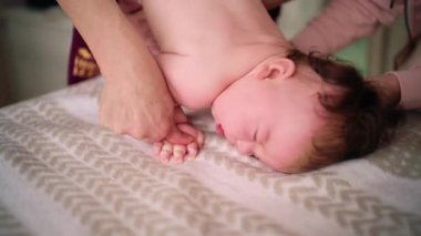 Bebek karnının üstünde yatarken bir yetişkin onlara masaj yapıyor ve hareket egzersizleri yapıyor.