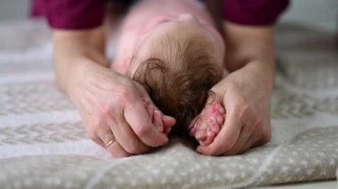 Bebek sırt üstü yatarken bir yetişkin onlara masaj yapıyor ve hareket egzersizleri yapıyor.