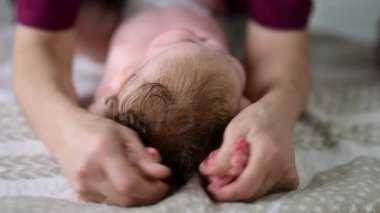 Bebek sırt üstü yatarken bir yetişkin onlara masaj yapıyor ve hareket egzersizleri yapıyor.