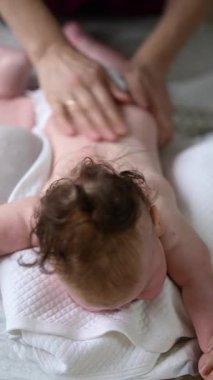 Bebek karnının üstünde yatarken bir yetişkin onlara masaj yapıyor ve hareket egzersizleri yapıyor.