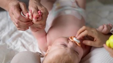 Bebek sırt üstü yatarken bir yetişkin onlara masaj yapıyor ve anne de emziği bebeğin ağzında tutuyor.