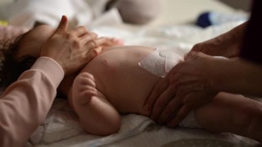 Bebek sırt üstü yatarken bir yetişkin onlara masaj yapıyor ve anne de emziği bebeğin ağzında tutuyor.