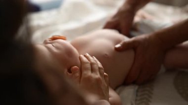 Bebek sırt üstü yatarken bir yetişkin onlara masaj yapıyor ve anne de emziği bebeğin ağzında tutuyor.