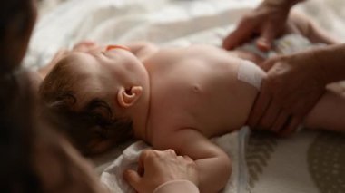 Bebek sırt üstü yatarken bir yetişkin onlara masaj yapıyor ve anne nazikçe bebeğin elini tutuyor.