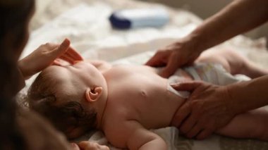 Bebek sırt üstü yatarken bir yetişkin onlara masaj yapıyor ve anne de emziği bebeğin ağzında tutuyor.