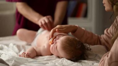 Bebek sırt üstü yatarken bir yetişkin onlara masaj yapıyor ve anne de emziği bebeğin ağzında tutuyor.