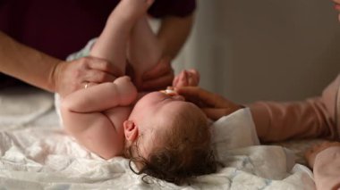 Bebek sırt üstü yatarken bir yetişkin onlara masaj yapıyor ve anne de emziği bebeğin ağzında tutuyor.