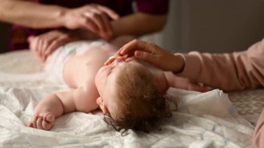 Bebek sırt üstü yatarken bir yetişkin onlara masaj yapıyor ve anne de emziği bebeğin ağzında tutuyor.