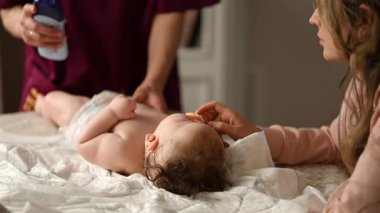 Bebek sırt üstü yatarken bir yetişkin onlara masaj yapıyor ve anne de emziği bebeğin ağzında tutuyor.