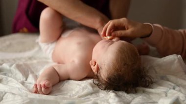 Bebek sırt üstü yatarken bir yetişkin onlara masaj yapıyor ve anne nazikçe bebeğin elini tutuyor.