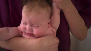 Bebek, bir bakıcının koluna yüz üstü uzanıyor, güvenli bir şekilde destekleniyor.