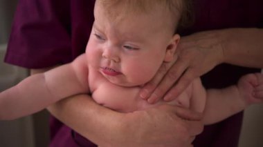 Bebek, bir bakıcının koluna yüz üstü uzanıyor, güvenli bir şekilde destekleniyor.