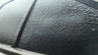 Buz ve buzla kaplı bir arabanın yan görüntüsü, kentsel arka planda desenli donmuş bir yüzey yaratıyor.