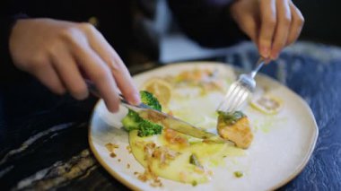 Brokoli ve sosla servis edilen somon filetosunu kesmek için çatal ve bıçakla ellerini kapat.