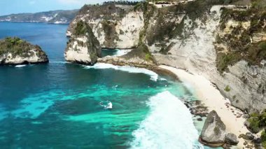 Diamond Beach 'in hava aracı görüntüsü ve Nusa Penida, Bali' deki ikonik off-shore kaya zirvesi. Güçlü okyanus dalgaları dramatik kireçtaşı kayalıkları ve yemyeşil tropikal bitki örtüsüyle karşılaşıyor