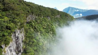 Alçak bulutlar ve vadiden yükselen sis ile dik bir yağmur ormanı uçurumu boyunca uçan drone görüntüsü, Madagaskar 'daki dramatik dağları ve el değmemiş tropikal doğayı gözler önüne seriyor.