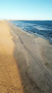 Namibya 'daki uzak İskelet Sahili kıyı şeridinin hava aracı görüntüsü geniş bir kumsal ve çöl kumulları boyunca dalgaların kırıldığını gösteriyor. Dikey