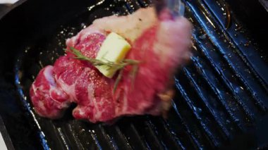 Tereyağı, baharatlı bir bifteğin üzerinde eriyor. Biberiye ile ızgara tavasında pişiyor.