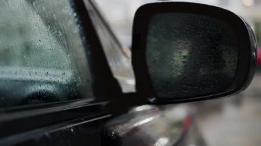 Yağmurlu havalarda araba yan aynası ve yağmur damlacıklarıyla kaplı ıslak pencereyi kapat