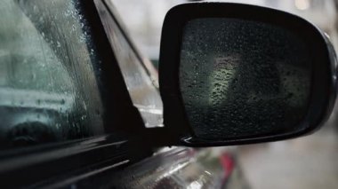Yağmurlu havalarda araba yan aynası ve yağmur damlacıklarıyla kaplı ıslak pencereyi kapat