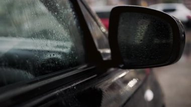 Yağmurlu havalarda araba yan aynası ve yağmur damlacıklarıyla kaplı ıslak pencereyi kapat