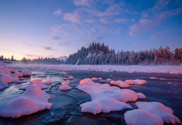 Winter dawn in mountains. Mountain landscape with river covered with ice. Winter scenic background with clear blue sky and white snow.