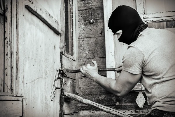 O ladrão mascarado quebra a porta da fechadura na casa — Fotografia de Stock