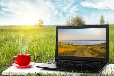 Laptop ve sıcak kahve üzerinde arka plan güzel doğa, açık ofis