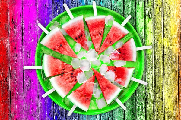 Dílek melounu s kostkami ledu na vícebarevné pozadí — Stock fotografie
