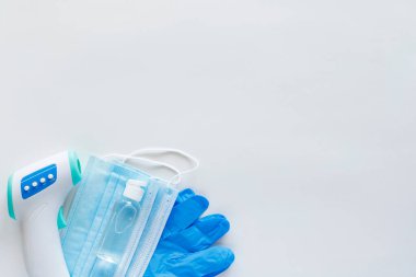 Corona virüsü koruma konsepti düzdü. Temassız kızılötesi vücut termometresi, lateks eldivenler, tek kullanımlık maskeler ve fotokopi alanı olan beyaz arka planda dezenfektan..