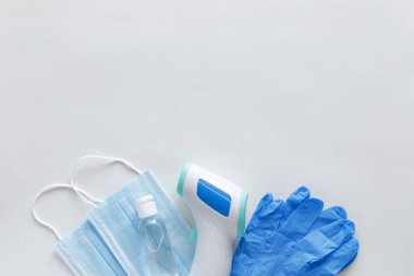 Corona virüsü koruma konsepti düzdü. Temassız kızılötesi vücut termometresi, lateks eldivenler, tek kullanımlık maskeler ve fotokopi alanı olan beyaz arka planda dezenfektan..