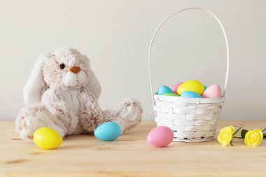 Paskalya oyuncak tavşanı, sepetli renkli yumurtalar ve beyaz arka planlı küçük çiçekler ve kopyalama alanı..