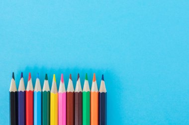 Mavi kağıt arka planında parlak renkli kalemler.