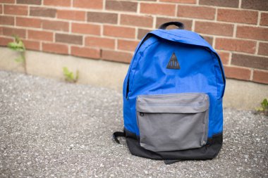 Okul sırt çantası yolda. Arkadaki okulun kırmızı tuğla duvarının yanındaki kaldırımda mavi çocuğun sırt çantası. Okula geri dönüş eğitim konsepti.