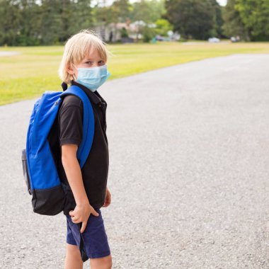Corona virüsü salgını sırasında maskeli bir çocuk. Maske takan ve sırt çantası taşıyan küçük bir çocuk okula gidiyor. Açılıştan sonra okul konseptine dönüş. Okul bahçesindeki öğrenci okul binasının yanında..