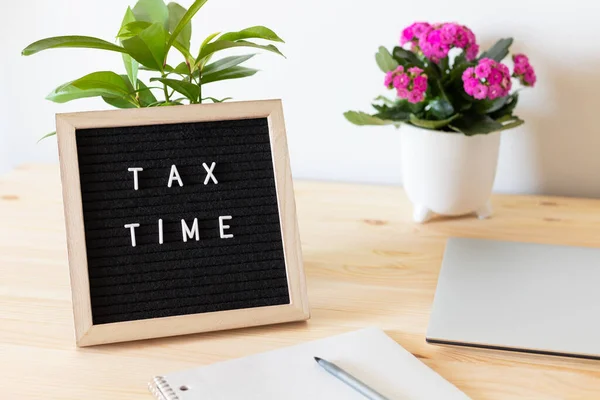 Tax time black felt letter board, laptop, notebook and flower pots on the table. Business tax return concept.