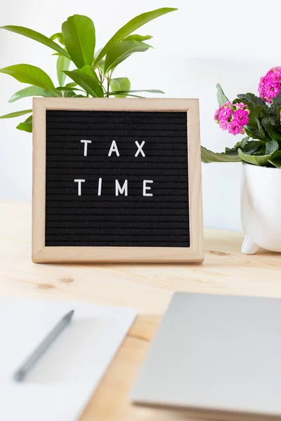 Tax time black felt letter board, laptop, notebook and flower pots on the table. Business tax return concept.