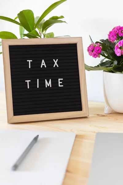 Tax time black felt letter board, laptop, notebook and flower pots on the table. Business tax return concept.