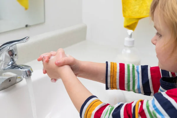 Little child washing hands with soap in the bashroom