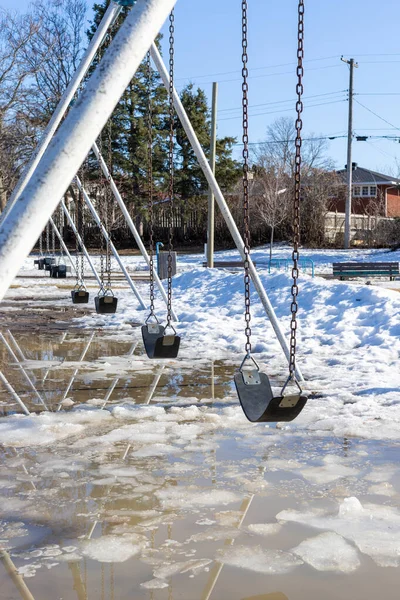 Early spring in the park with swings at the playground and dirty melting snow on the ground. Flooding during springtime.