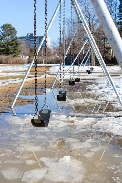 Early spring in the park with swings at the playground and dirty melting snow on the ground. Flooding during springtime.