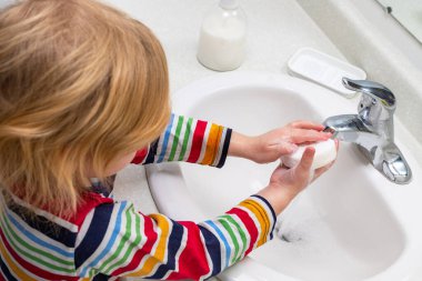 Küçük çocuk banyoda ellerini sabunla yıkıyor.