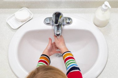 Küçük çocuk banyoda ellerini sabunla yıkıyor.