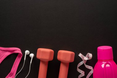 Dambıllar, mezura, su şişesi, kulaklık ve siyah arka planda spor giysisi. Fitness, spor ve egzersiz konsepti fotokopi alanı ile düz yatıyordu.