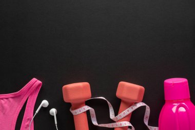 Dambıllar, mezura, su şişesi, kulaklık ve siyah arka planda spor giysisi. Fitness, spor ve egzersiz konsepti fotokopi alanı ile düz yatıyordu.