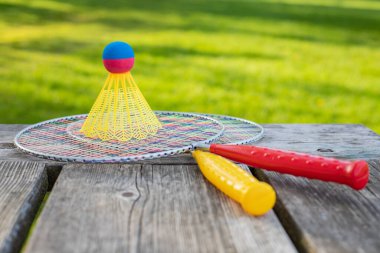 Badminton oyun raketleri ve tahta masadaki mekik horozu güneşli bir yaz gününde parkta yeşil çim arka planda. Aktif yaşam tarzı konsepti. Bir aile için açık havada eğlenceli aktiviteler.