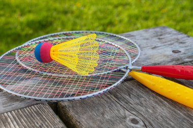 Badminton oyun raketleri ve tahta masadaki mekik horozu güneşli bir yaz gününde parkta yeşil çim arka planda. Aktif yaşam tarzı konsepti. Bir aile için açık havada eğlenceli aktiviteler.