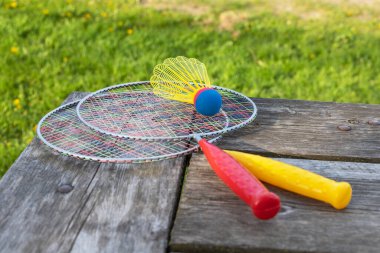 Badminton oyun raketleri ve tahta masadaki mekik horozu güneşli bir yaz gününde parkta yeşil çim arka planda. Aktif yaşam tarzı konsepti. Bir aile için açık havada eğlenceli aktiviteler.